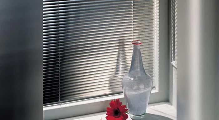 Dark aluminum blinds covering a window beside a vase