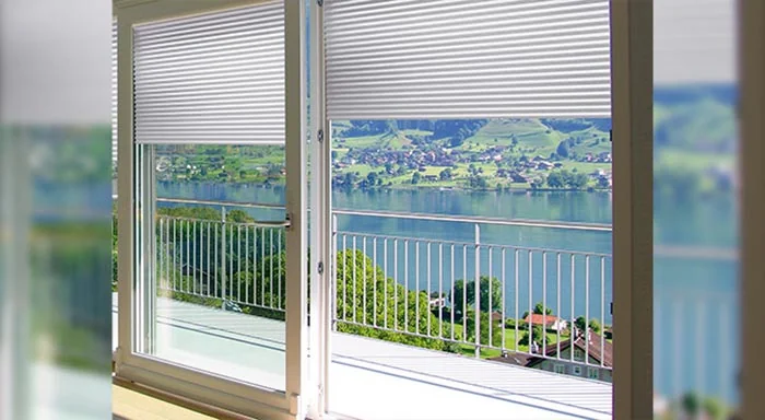 Cellular shades partially lowered over lakeside windows
