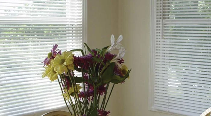 White aluminum blinds behind a vase of flowers